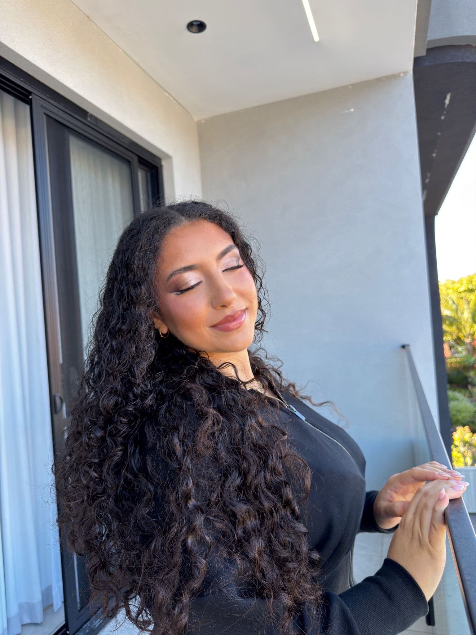 Client with long curls, soft bronze glam, eyes closed in golden light